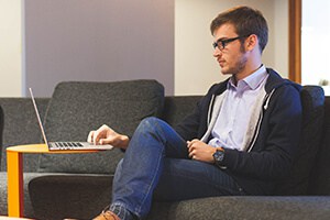 man sitting on couch scrolling through his laptop