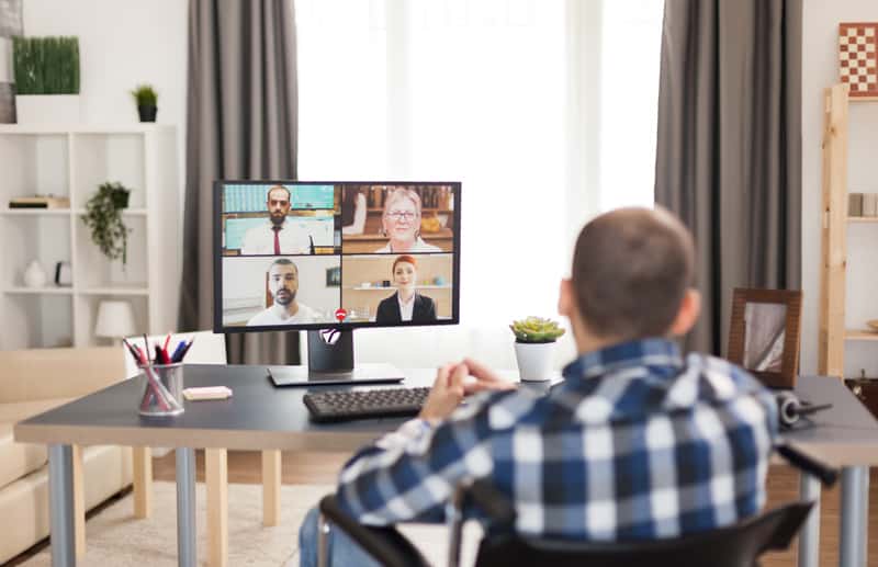 man at a desk speaking with a breakout room of four people