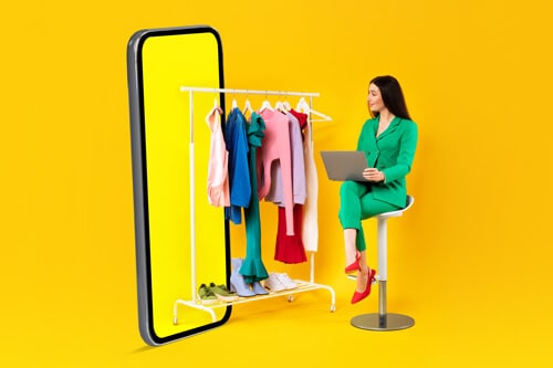 a shop owner sitting next to a rack of clothes and a giant phone representing the future of e-commerce online