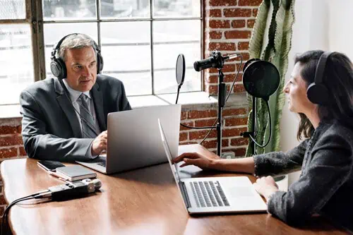 a woman with a business podcast interviewing a man about his company's success in a room with a window