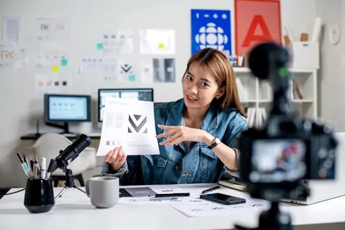 a young woman showing off her designs in front of a recording camera to go on a business podcast