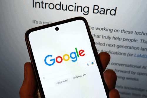 google search engine on a phone in front of a computer screen showing Bard 