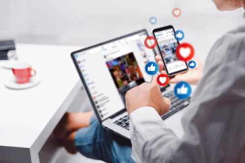 a person looking at their phone and computer with social media platform pulled up thinking about social media and business growth for the company